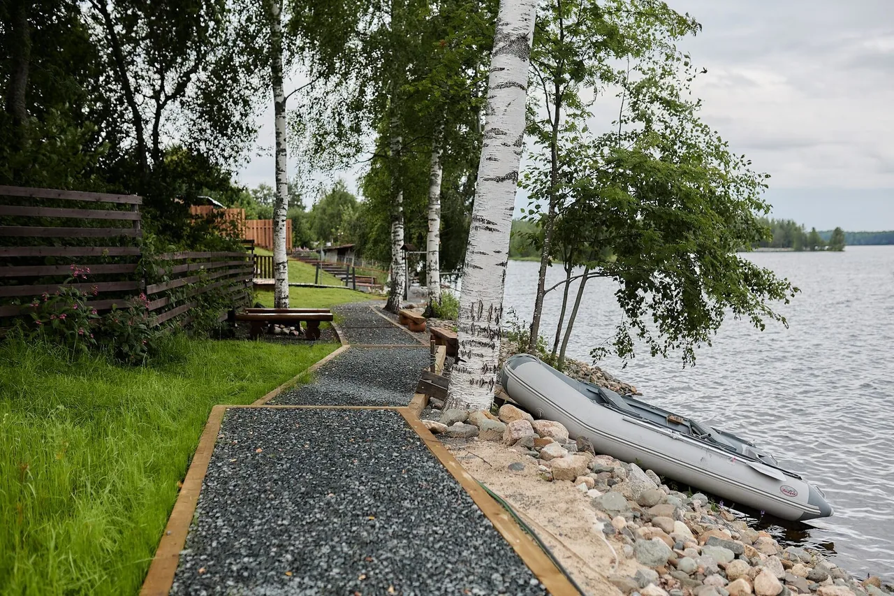 Гравийная дорожка вдоль берега между берёз, у воды лежит лодка — глэмпинг «4 стихии»